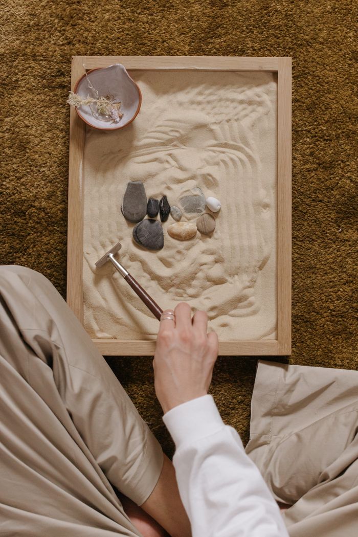 services-01 A calming zen garden setup with sand and rocks, featuring a hand arranging with a rake.